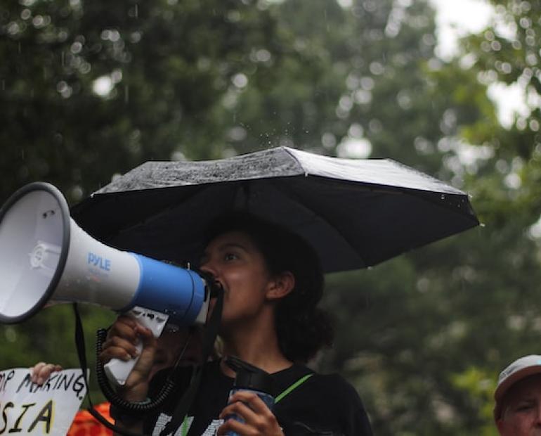 Women standing under umbrella and speaking into a megaphone