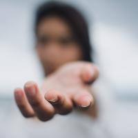 A person reaches out a hand towards the camera. The person is blurred and only the fingers of the hand are in focus