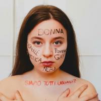 A young adult is posing straight in front of the camera, words such as "poor", "disabled", "gay" and others are written on her face. On her shoulders, you can read: "Are we all really equal?". Every word is written in Italian.
